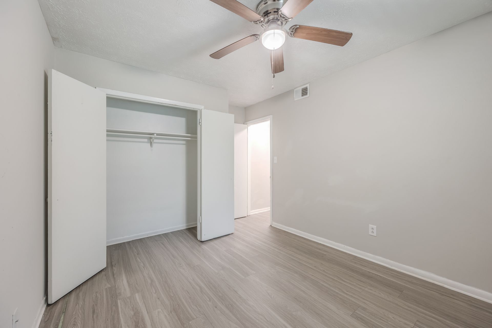 Ranch-style house with brick and gray exterior, pillars, surrounded by greenery and lawn.