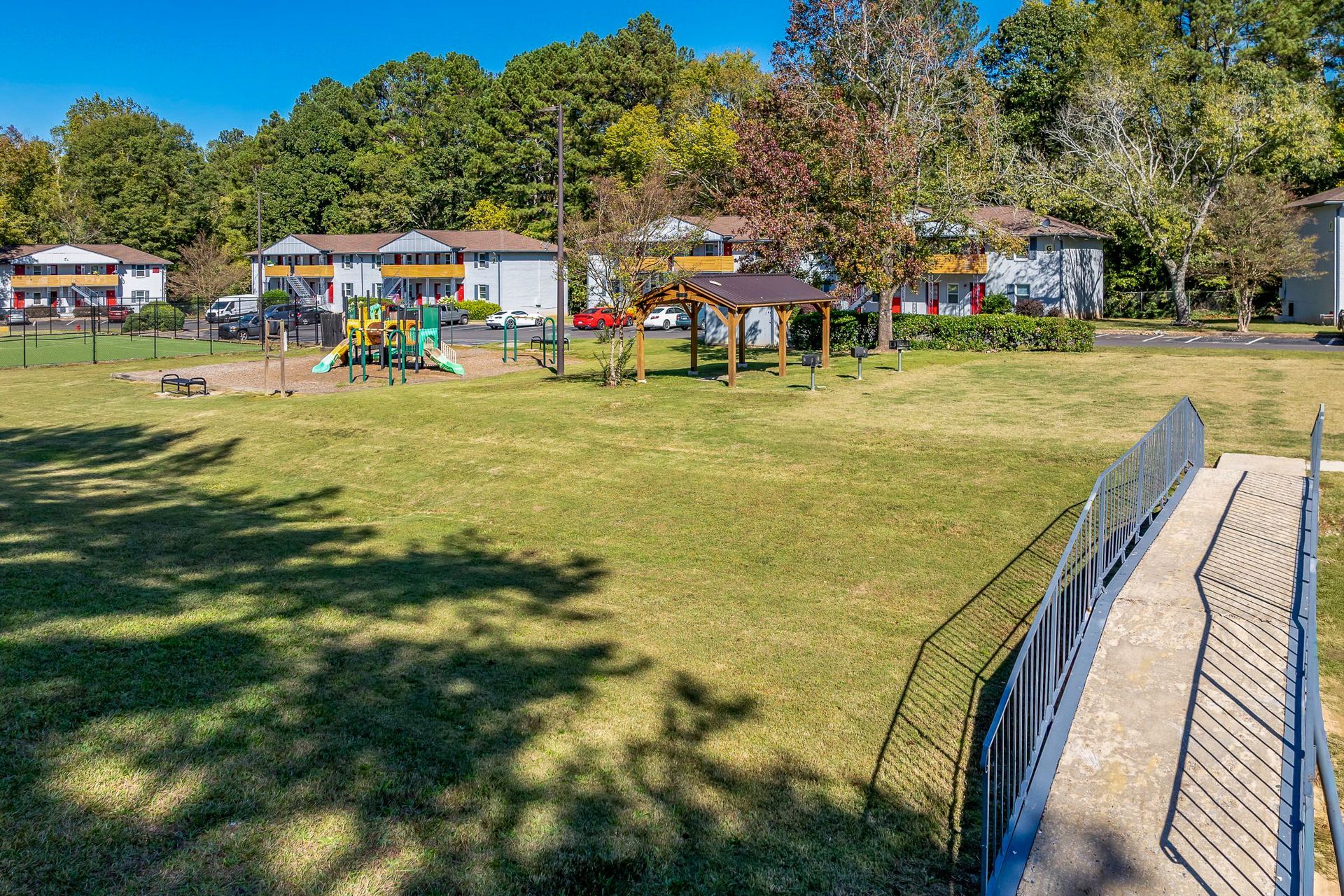 Ranch-style house with brick and gray exterior, pillars, surrounded by greenery and lawn.