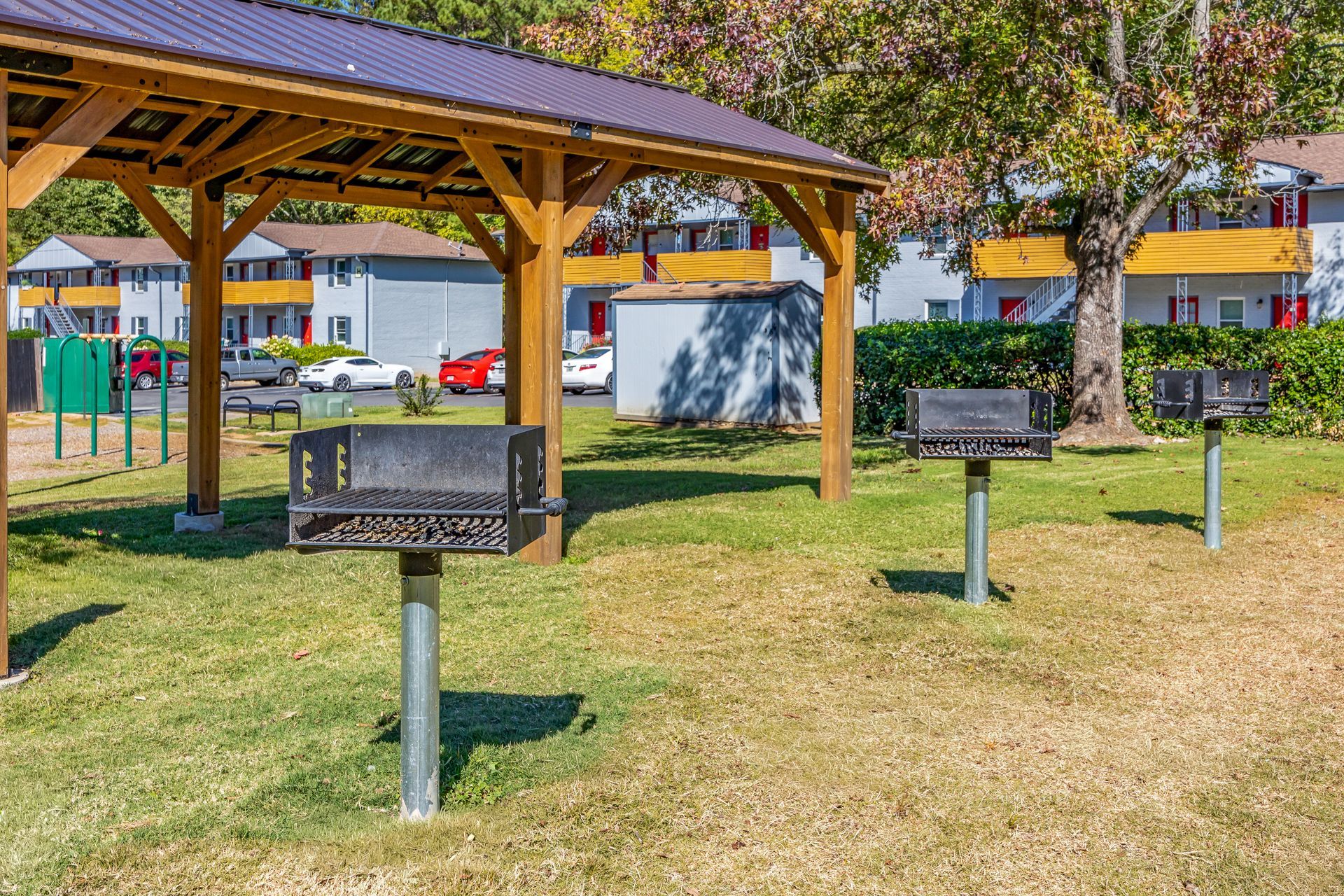 Park area with picnic shelter and three grills in front of apartment buildings.