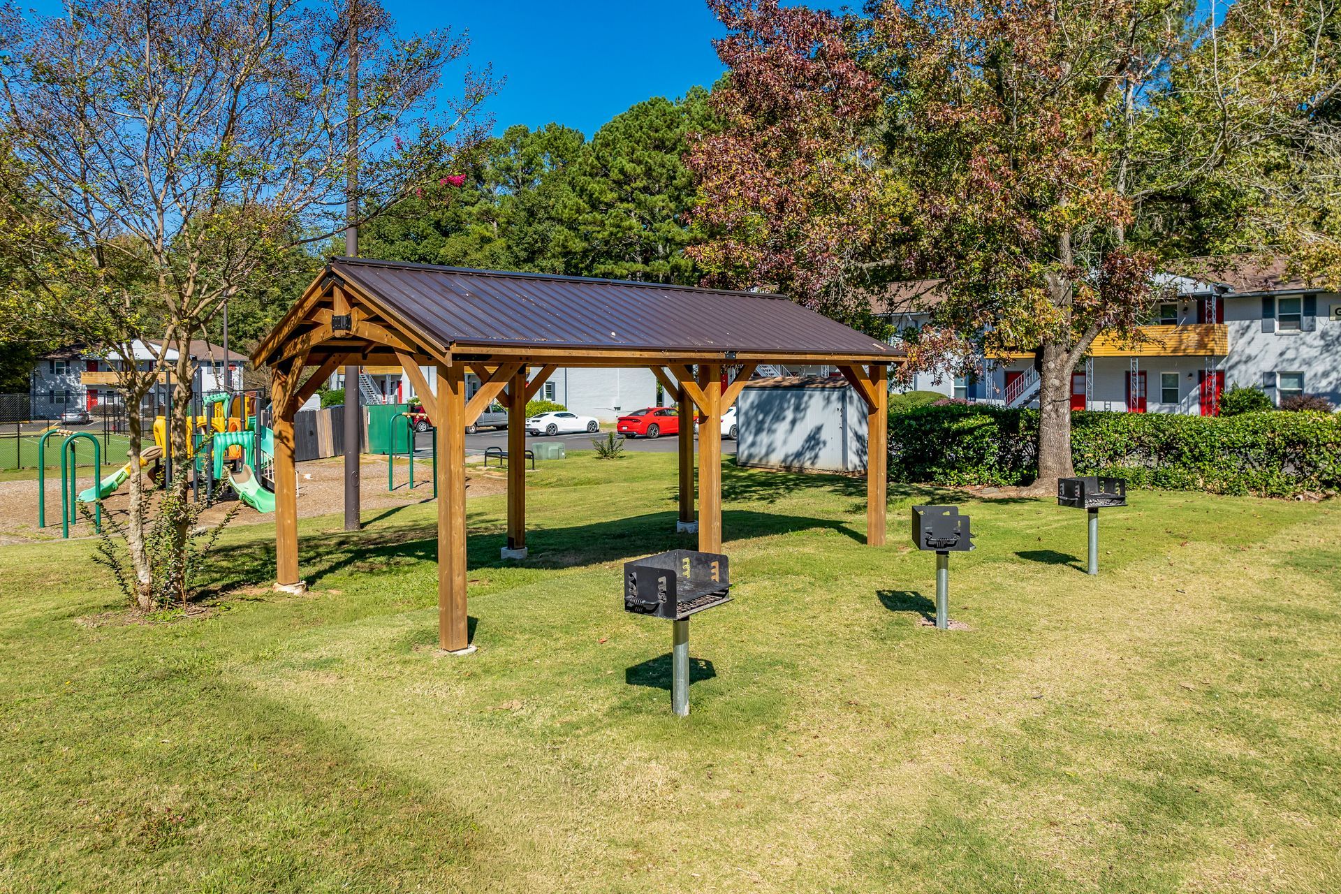 Playground with slides, tunnels, and climbing structures on a wood chip surface, surrounded by trees.