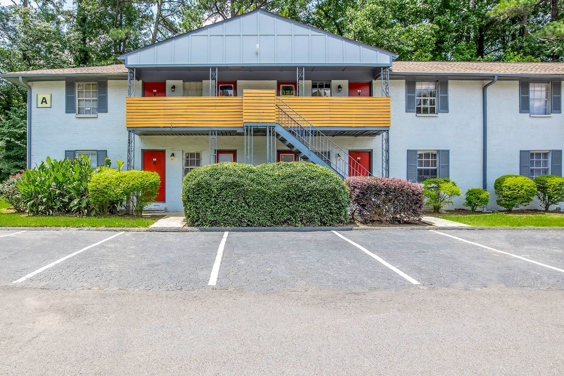 Ranch-style house with brick and gray exterior, pillars, surrounded by greenery and lawn.