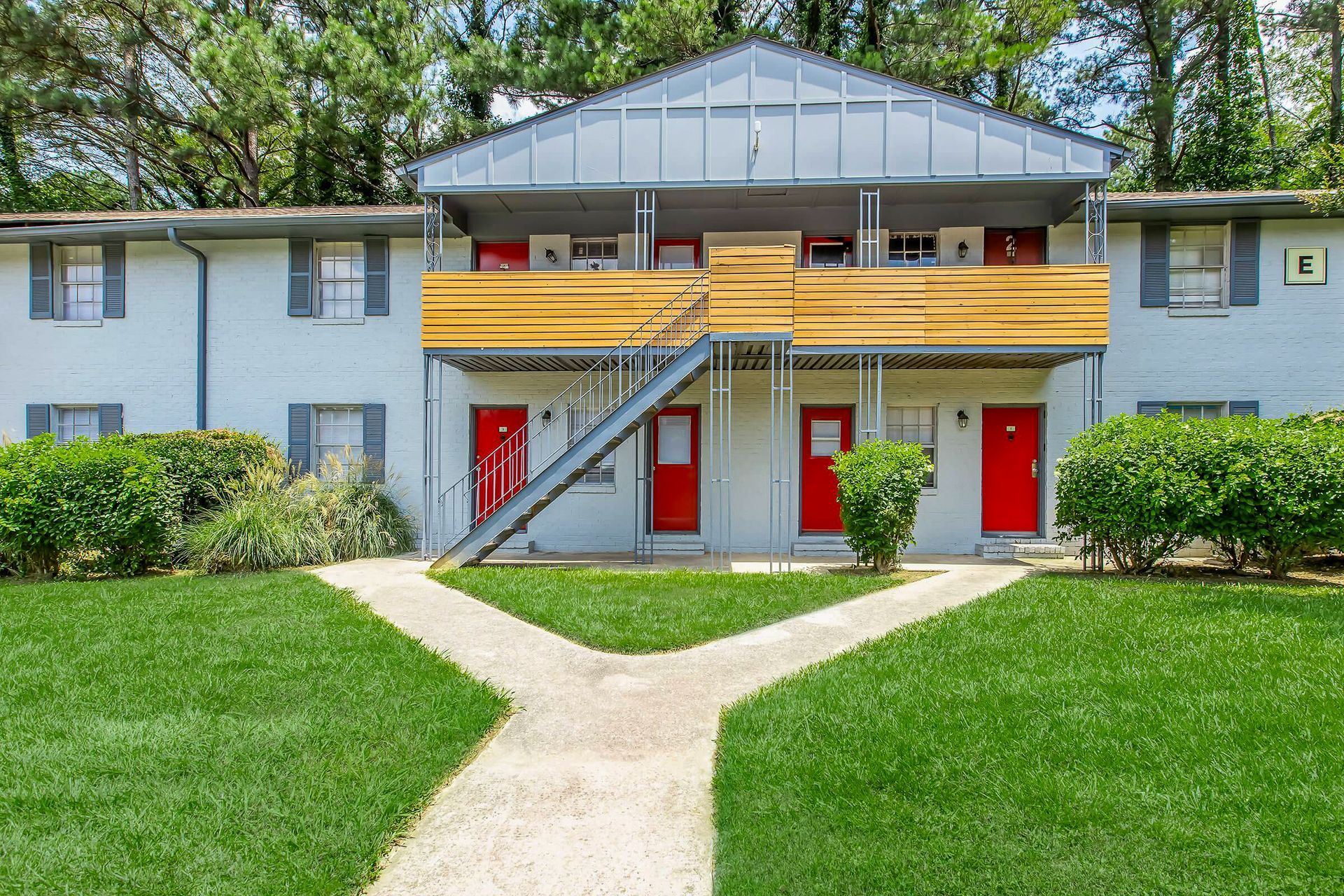 Ranch-style house with brick and gray exterior, pillars, surrounded by greenery and lawn.
