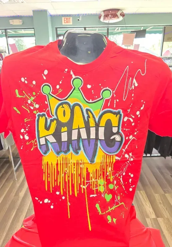 Red shirt with colorful graffiti-style “KING” text and paint drips, displayed indoors.