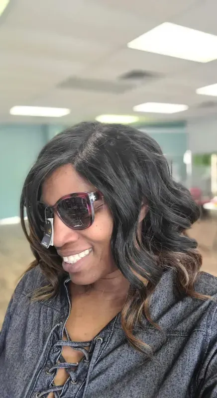 Person smiling in sunglasses with wavy hair in a brightly lit office setting