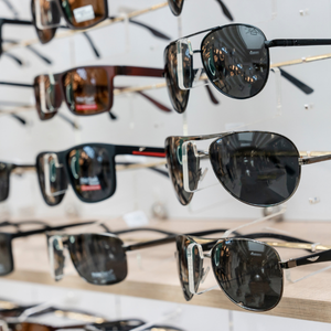 Rows of sunglasses displayed on shelves in a store, with dark tinted lenses and various frame styles