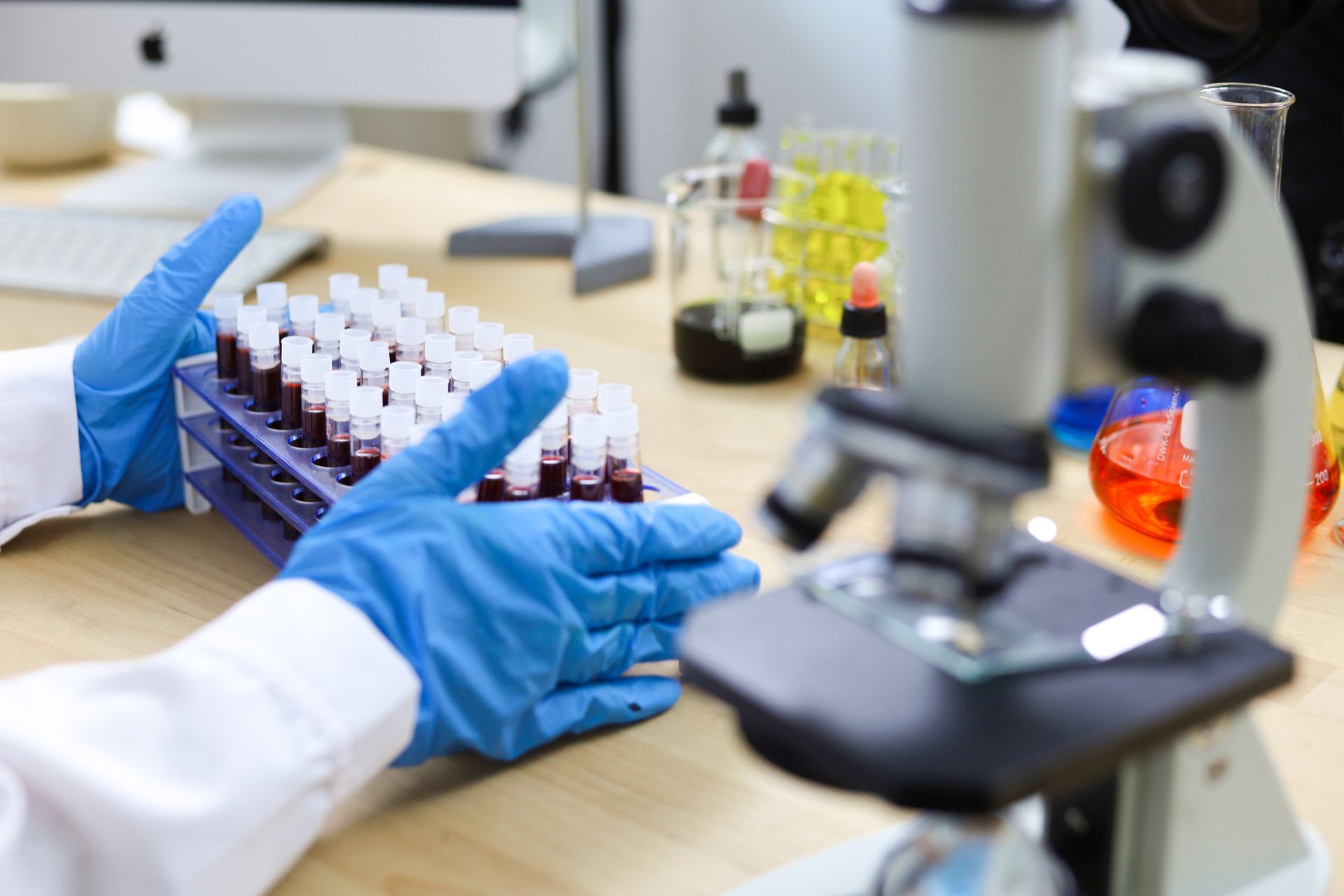 Uno scienziato tiene in mano un vassoio di provette davanti a un microscopio.