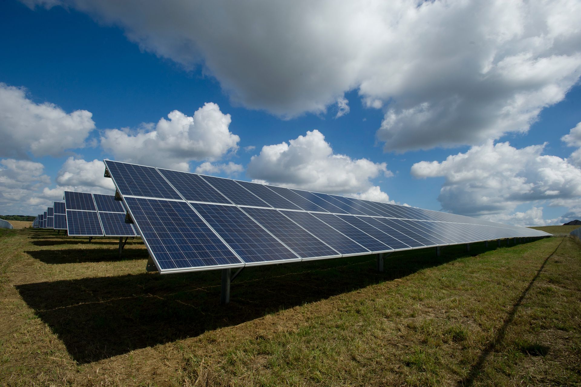 a row of solar panels in a field with clouds in the sky