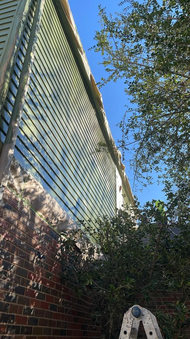 Brick wall next to a building with green siding and a ladder. Clear blue sky.