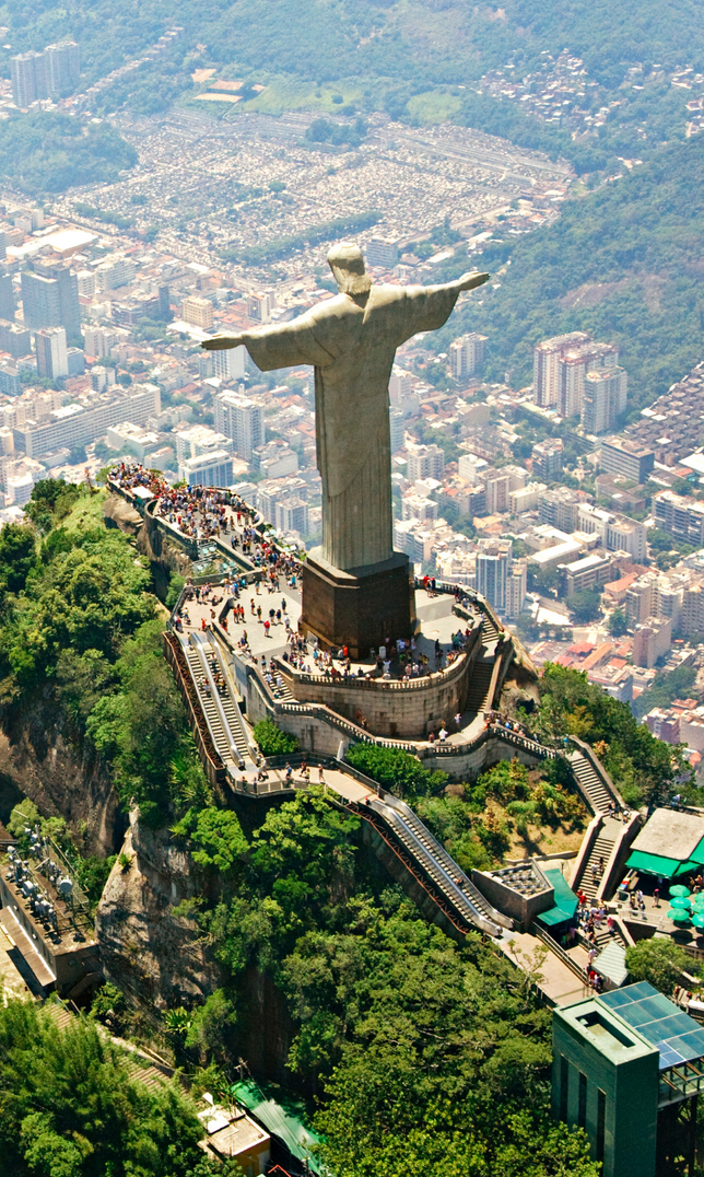 A large statue of jesus is sitting on top of a hill overlooking a city.