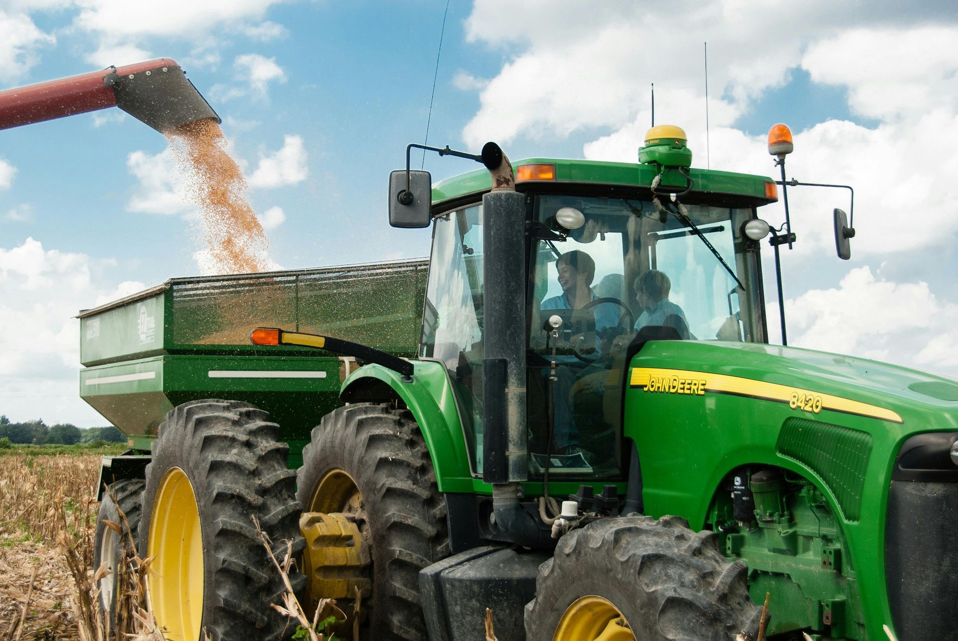 A man is driving a green john deere tractor in a field