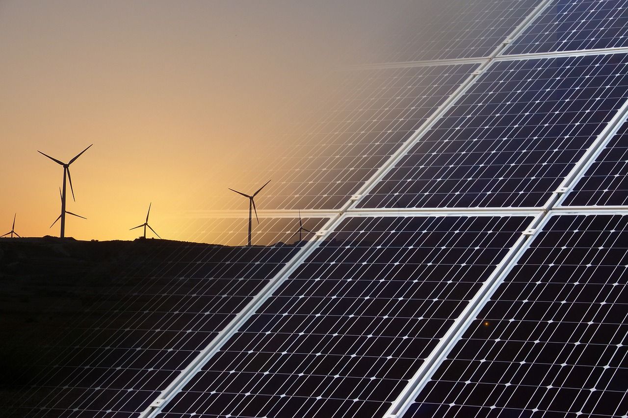 A sunset with solar panels and wind turbines in the background