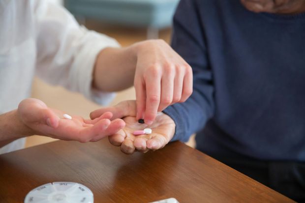 A person helping another take medication, placing pills into an open hand.