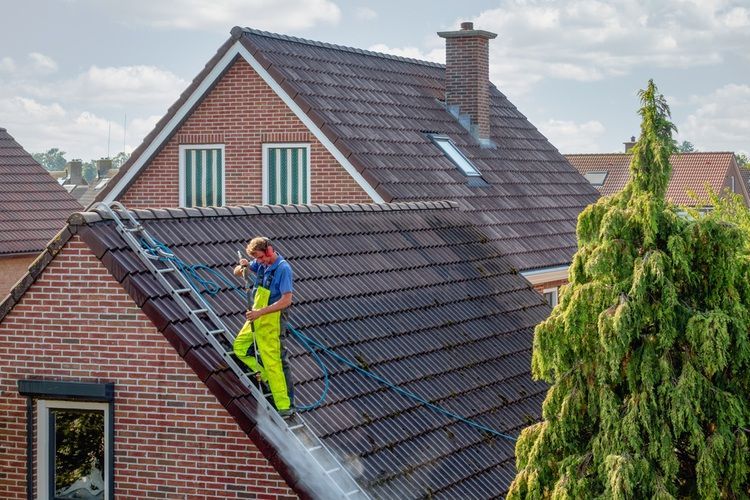 Why Is Soft Washing Safer for Roof Cleaning?  Cleaner with pressure washer at roof of house cleaning