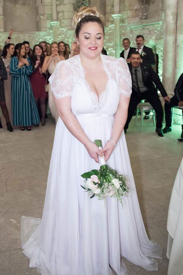 Une mariée grande taille dans une robe de mariée blanche tient un bouquet de fleurs.