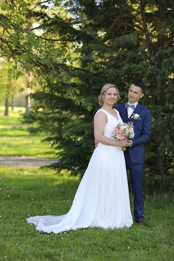 Une mariée et un marié posent pour une photo devant un arbre dans un parc.