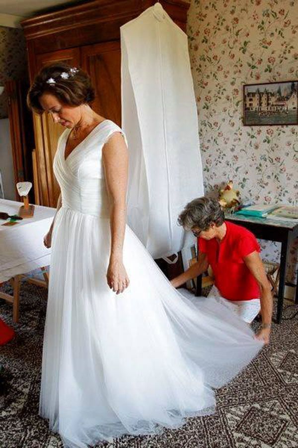 Une femme aide une femme à enfiler une robe de mariée.