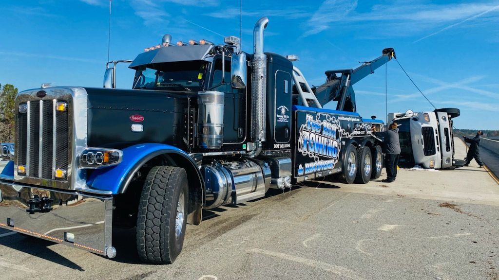 A tow truck is towing a vehicle that has fallen over on the side of the road.
