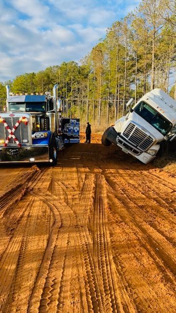 Two semi trucks are stuck in the mud on a dirt road.