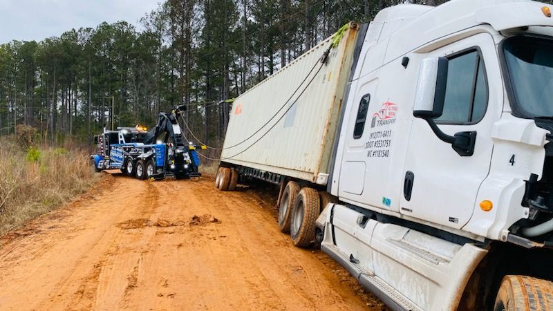 A semi truck is stuck in the mud on a dirt road.