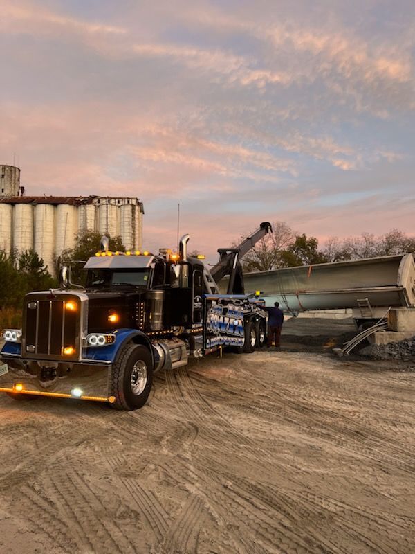 A semi truck is carrying a large piece of metal in a dirt field.