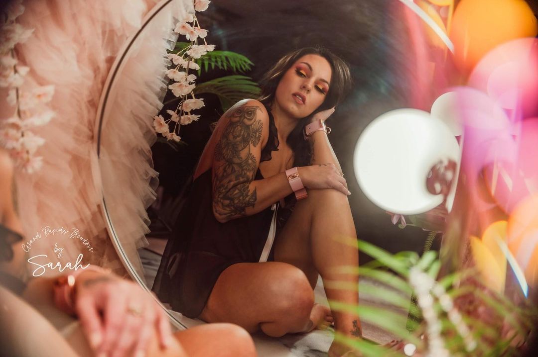 A woman is sitting in front of a mirror looking at herself.