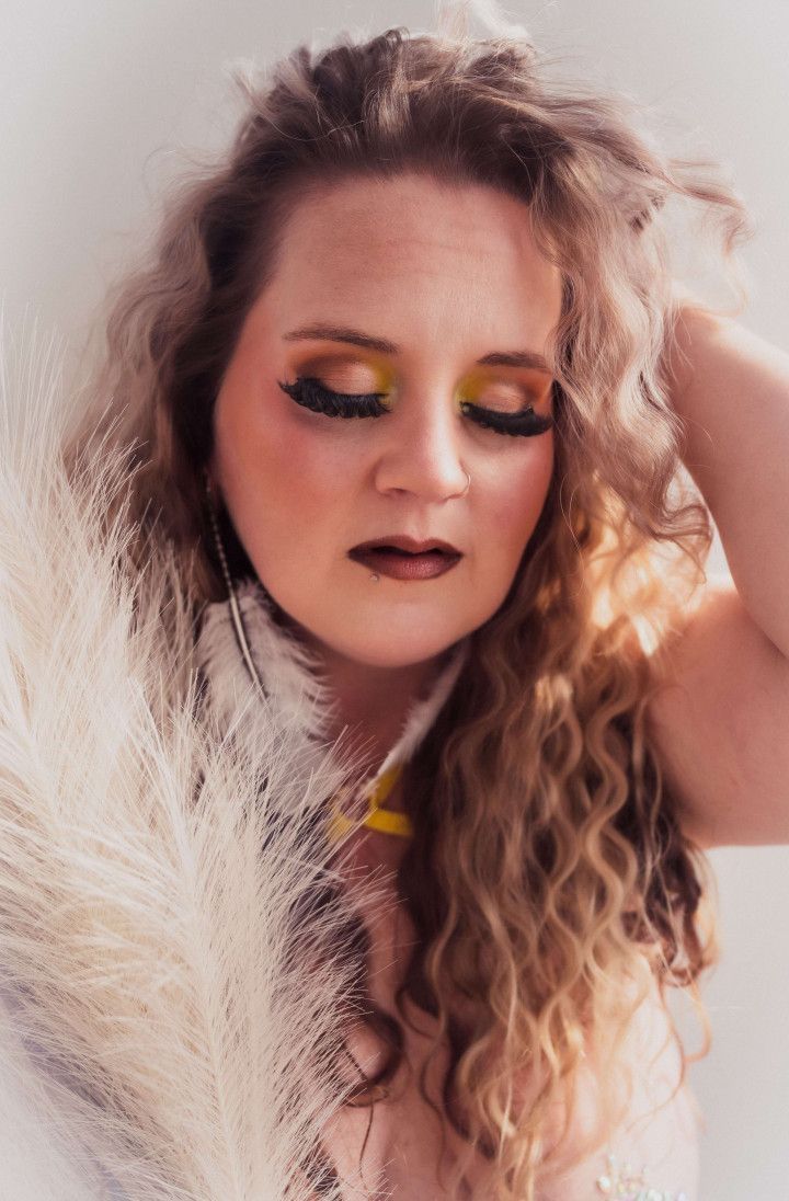 A woman with long curly hair is holding a pampas grass in her hand.