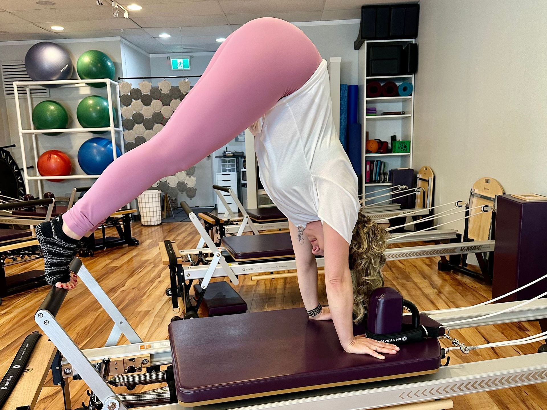 A woman is doing a handstand on a pilates machine in a gym.