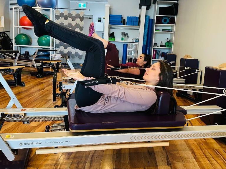 A woman is laying on a pilates machine in a gym.