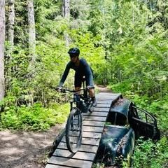 A man is riding a bike on a wooden bridge in the woods.