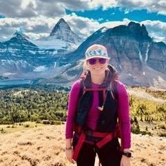 A woman with a backpack is standing in front of a mountain.