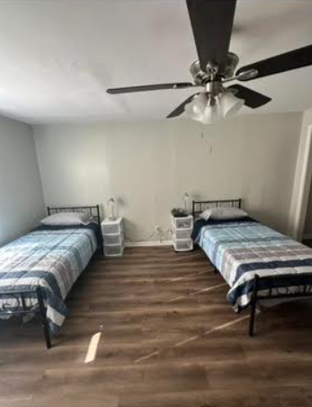 Two twin beds in a room, each with a bedside table, ceiling fan above.