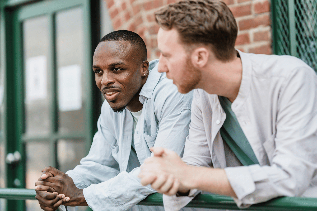 Two men leaning on a railing, chatting. One is Black, the other is white, both in light shirts.