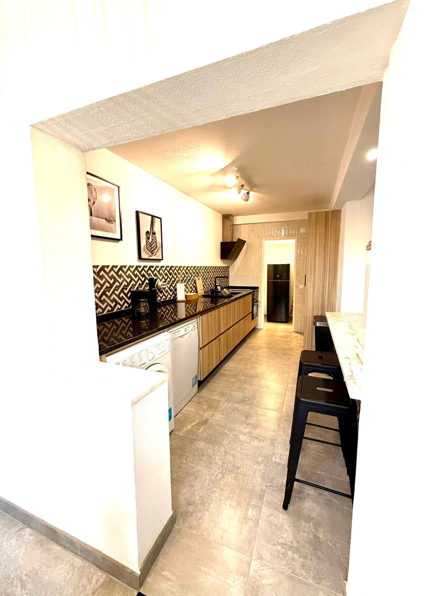 Moderne keuken met zwarte aanrechtbladen, houten kasten en een achterwand met tegelmotief.