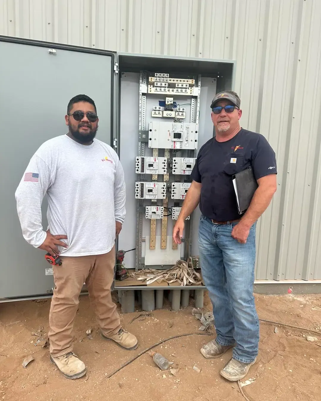 Two men are standing next to each other in front of an electrical box.