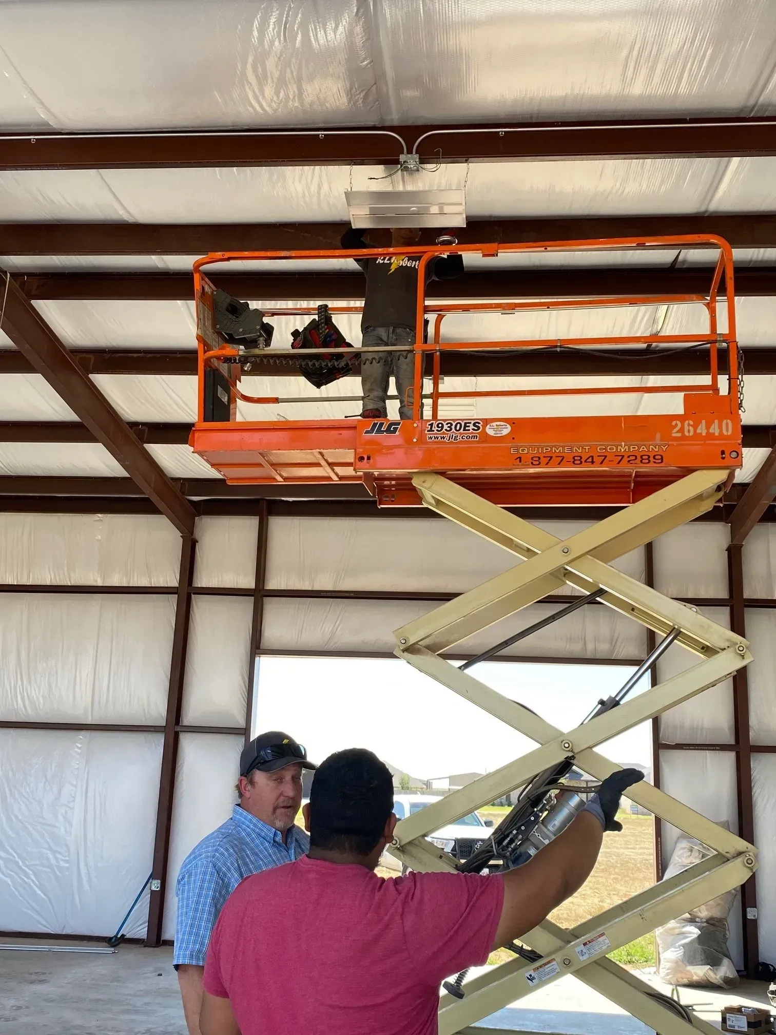 Two men are working on a scissor lift in a building.