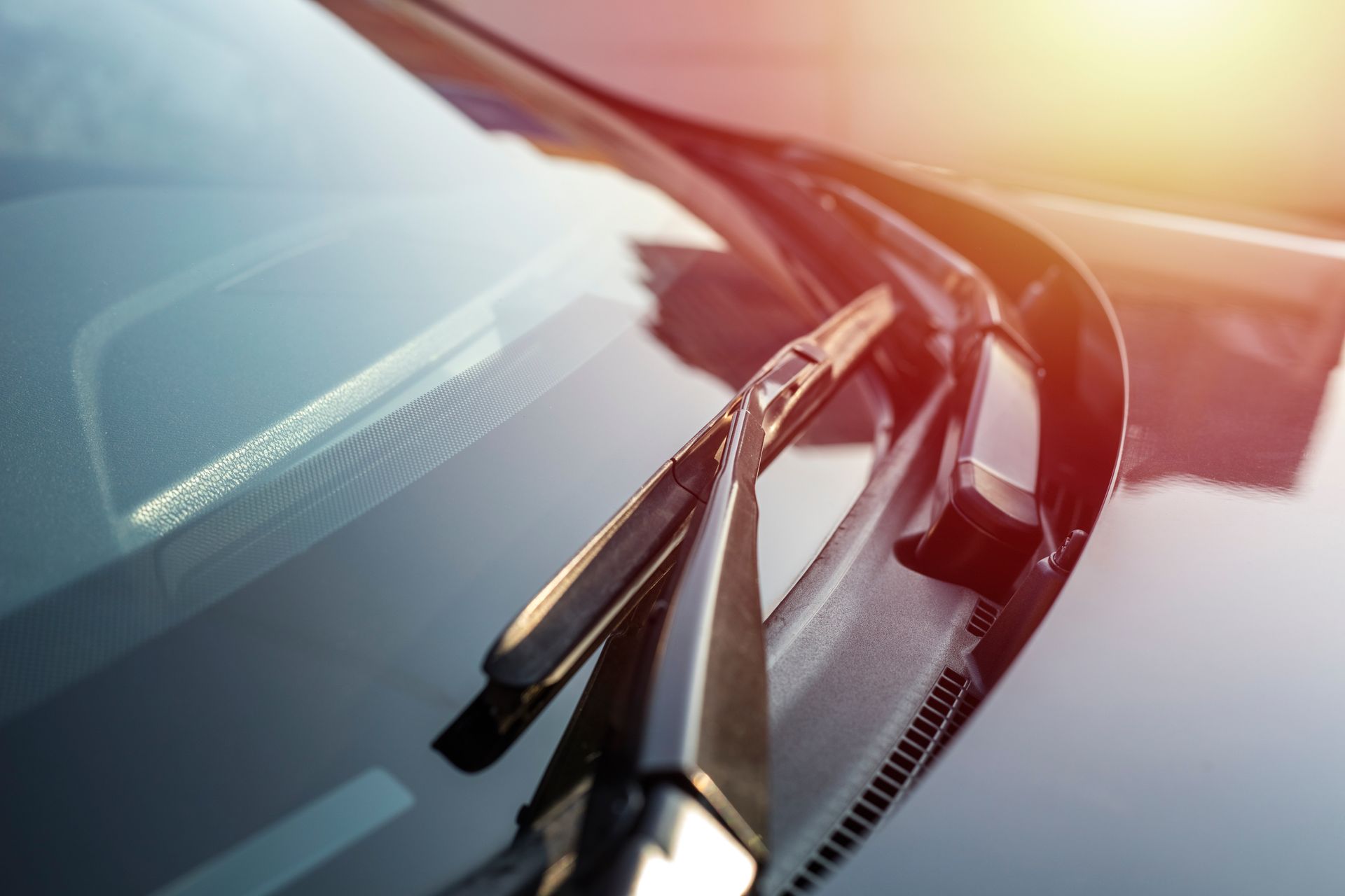 A close-up view of a car's windshield and wiper blade under warm, natural sunlight.