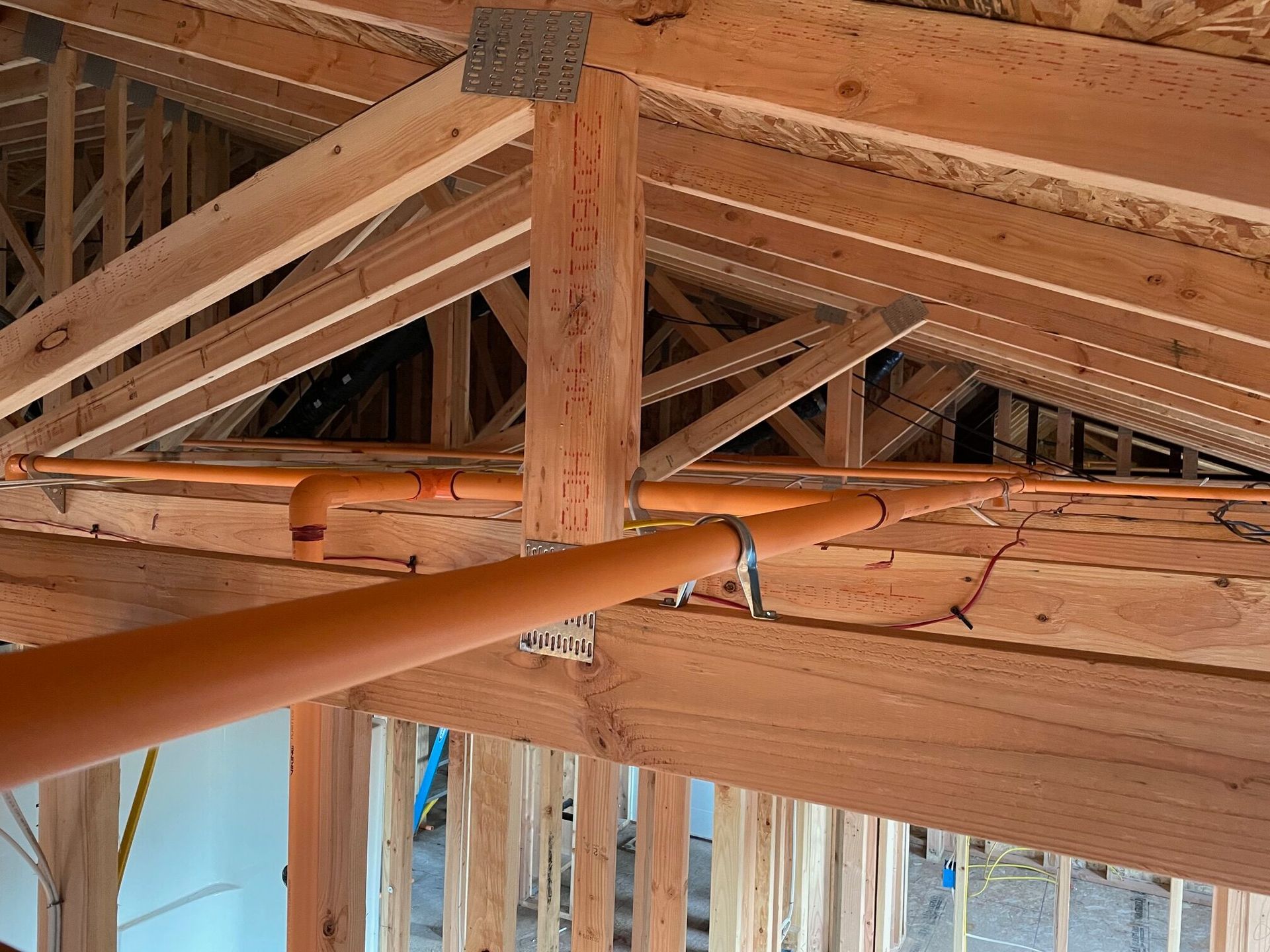 A house is being built with wooden beams and pipes hanging from the ceiling.