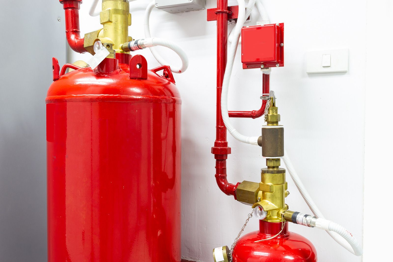 A red fire extinguisher is sitting next to a red pipe on a wall.