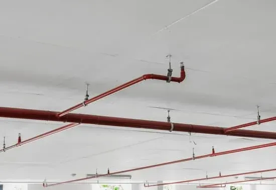 There are many red pipes hanging from the ceiling in a parking garage.