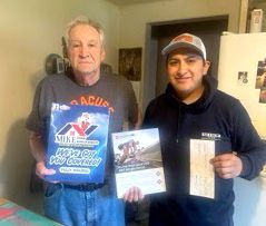 Two men are standing next to each other in a kitchen holding books.