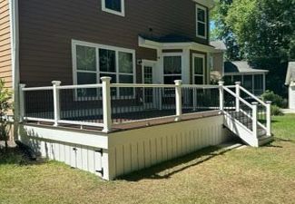 A large deck with a white railing is in front of a brown house.