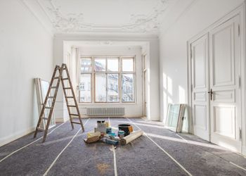 An empty room with a ladder and paint supplies on the floor.