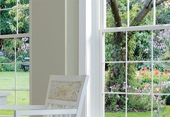 A white chair is sitting in front of a window with a view of a garden.