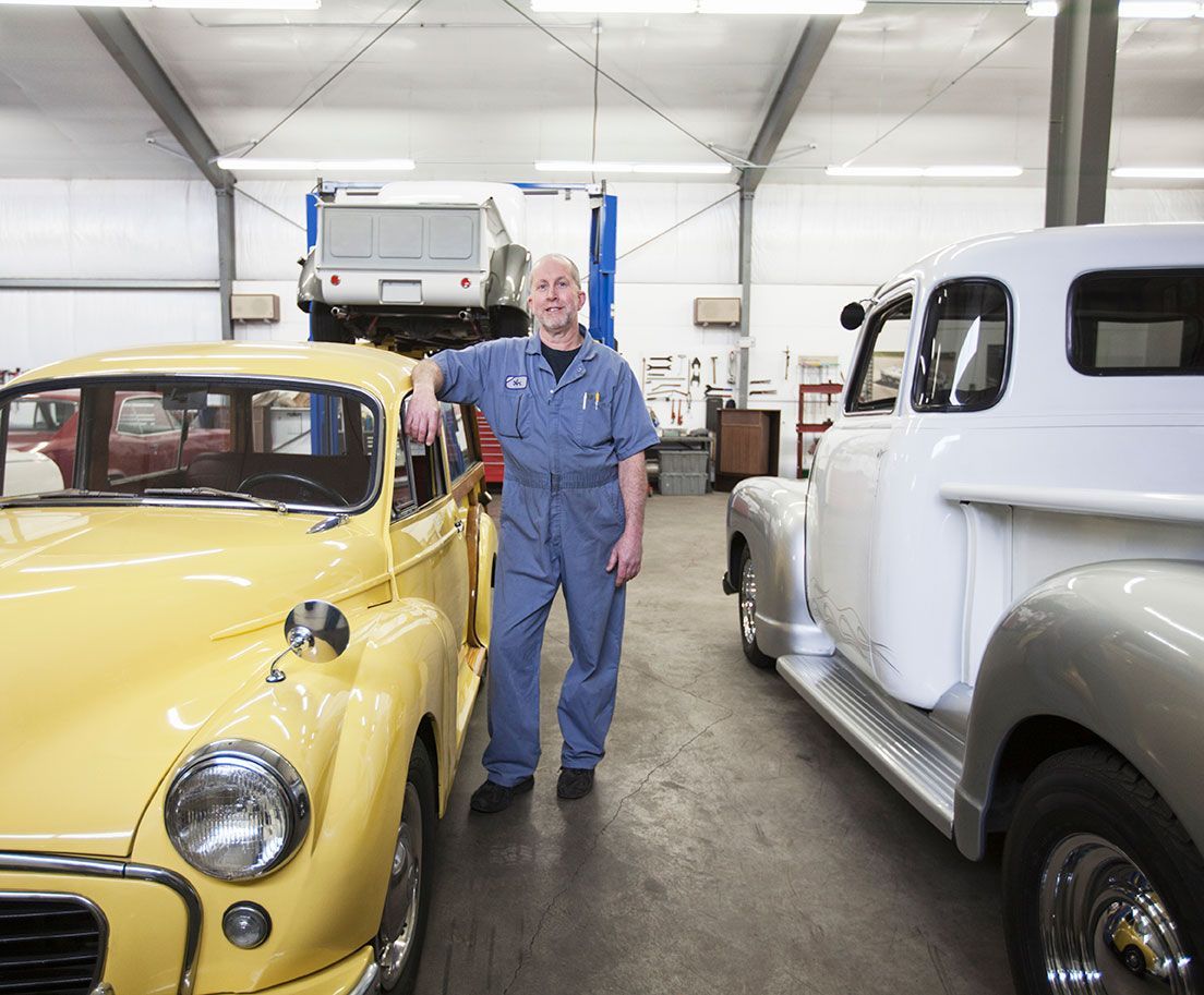 Woman in white blazer leans on a black electric car, smiling while on a call, solar panels in the background.