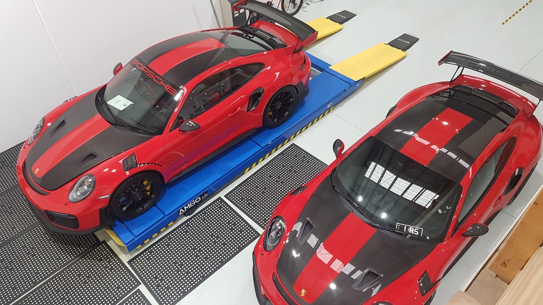 Two red Porsche 911 GT2 RS cars with black stripes are parked in a garage