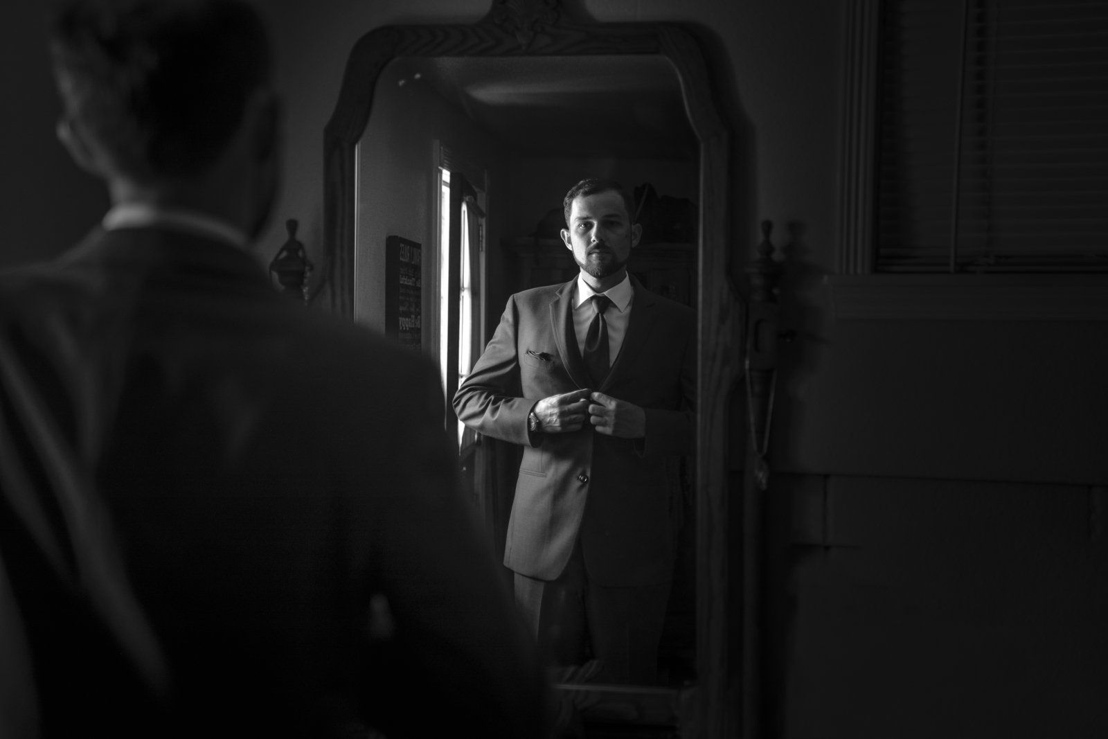 A man in a suit and tie is looking at himself in a mirror.