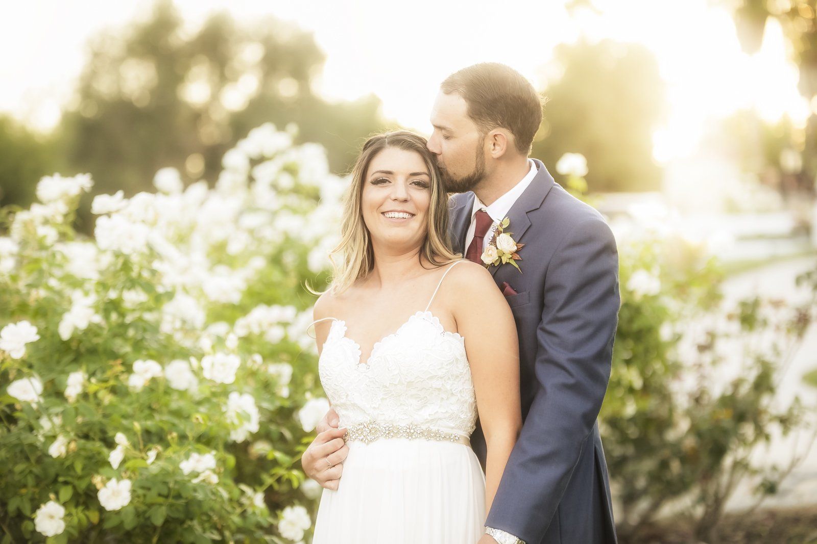 A bride and groom are posing for a picture in front of a bush of white flowers.