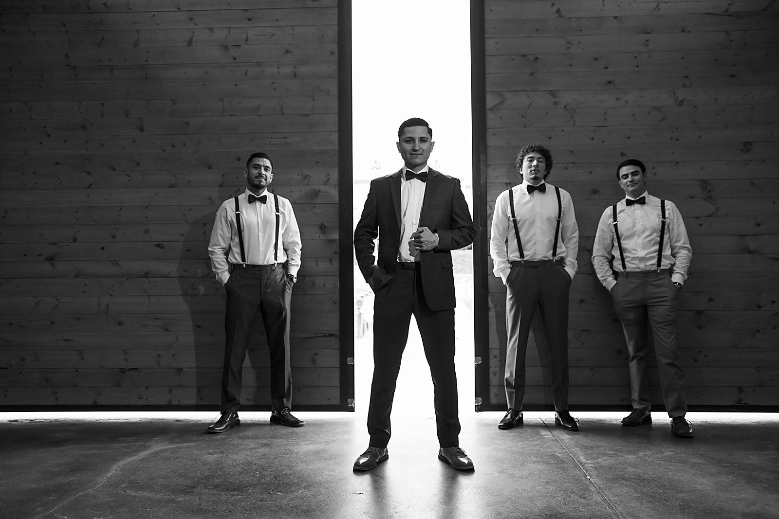A man in a suit and bow tie is standing in front of a group of men in suspenders.