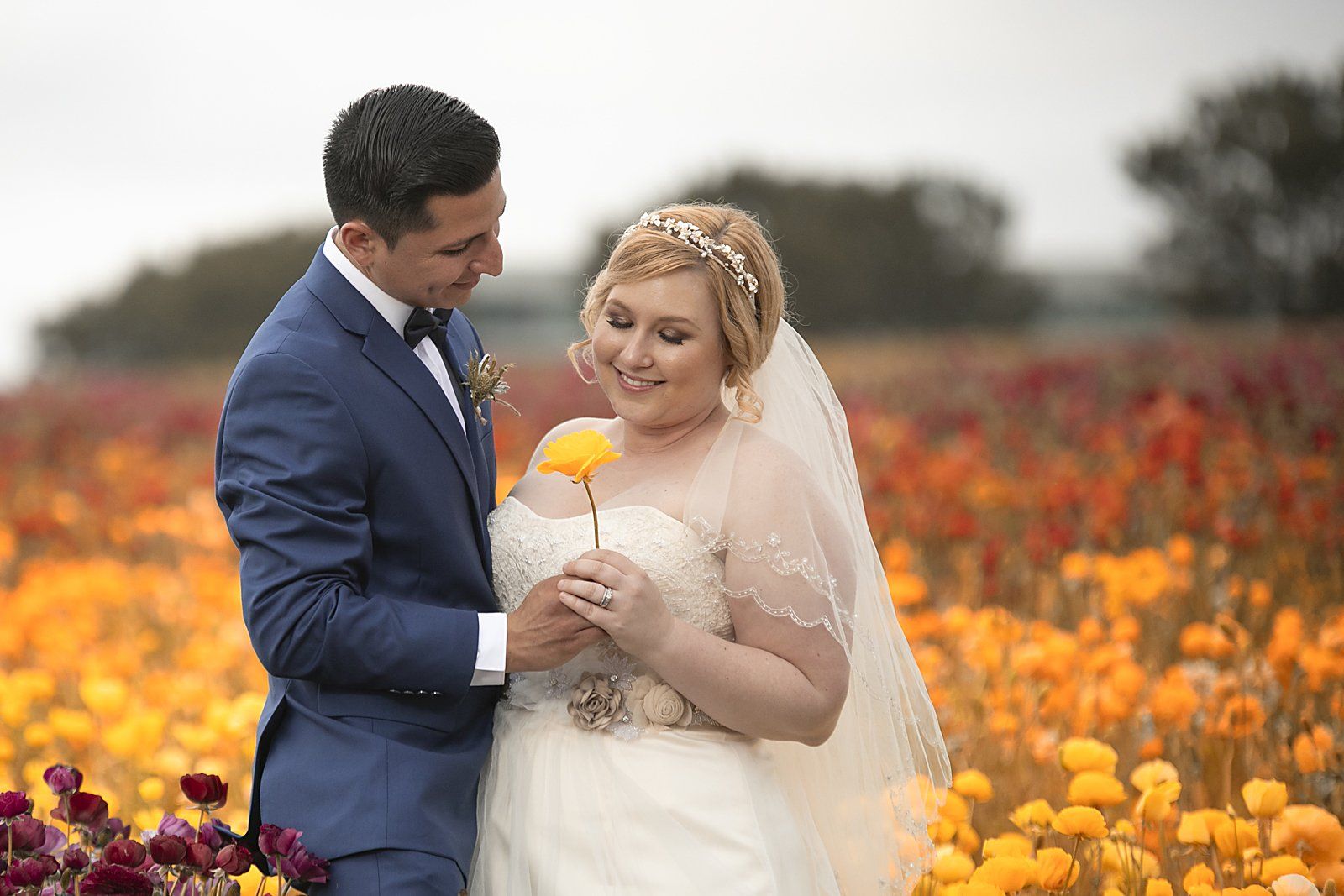 A bride and groom are posing for a picture in a field of flowers.