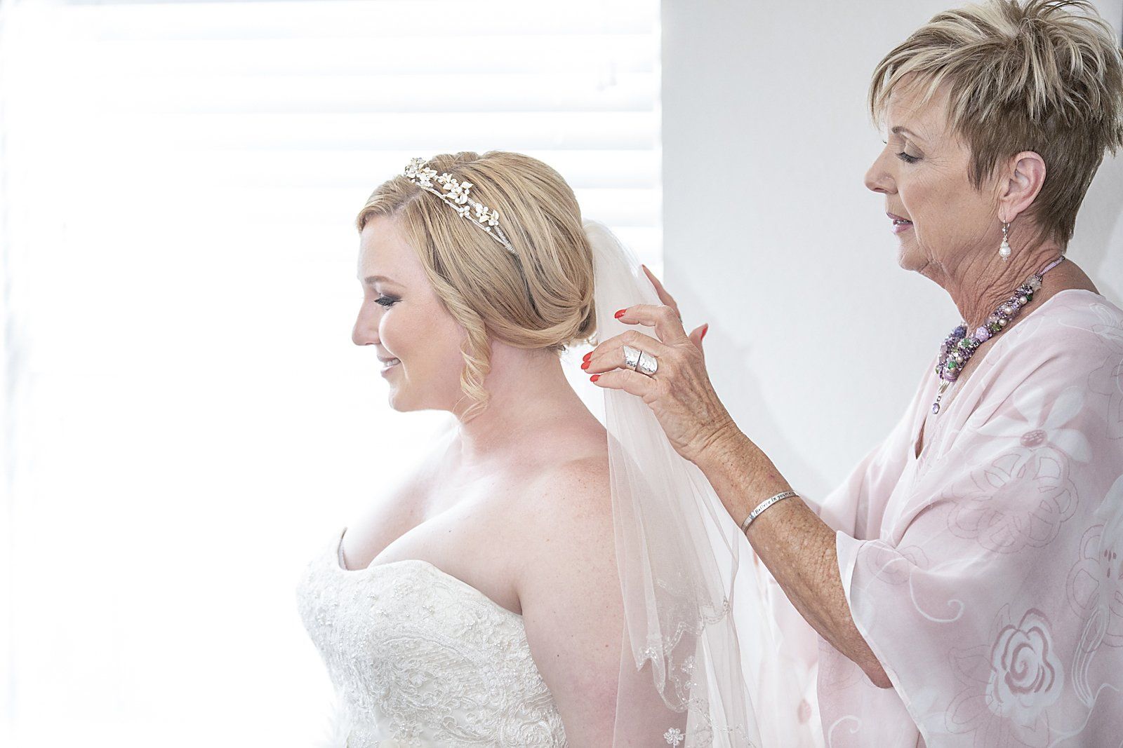 A woman is putting a veil on a bride 's head.